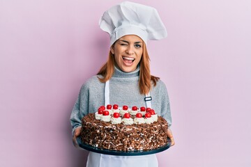Hispanic young chef woman holding chocolate cake winking looking at the camera with sexy...