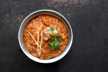 A top view of tikka masala, an oriental dish, on a black stony background. Spicy and sour curry with coriander, meat, cheese or fish, served with a rice. Traditional Indian, Pakistani cuisine.
