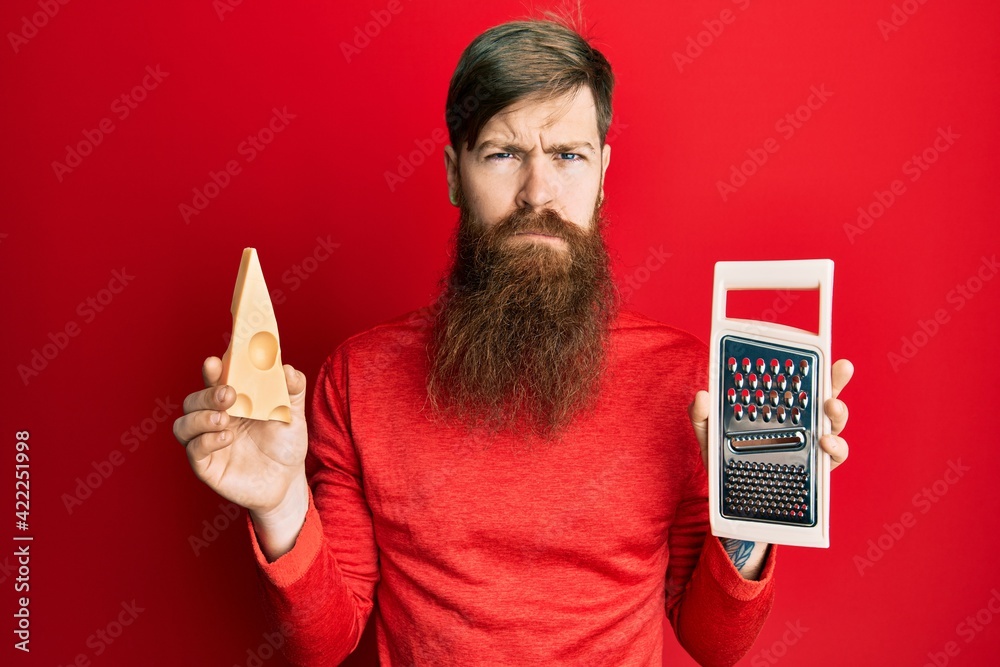 Wall mural redhead man with long beard holding grater and cheese skeptic and nervous, frowning upset because of