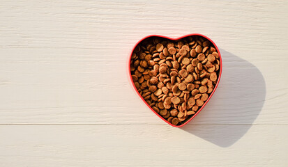 Food for pets in bowl of heart shape on wooden background with sunlight, top view, copy space