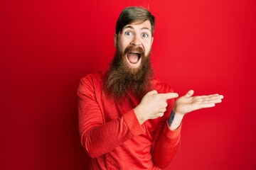 Redhead man with long beard pointing open palm with finger celebrating crazy and amazed for success with open eyes screaming excited.