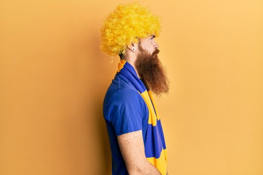 Redhead man with long beard football hooligan cheering game wearing funny wig looking to side, relax profile pose with natural face with confident smile.