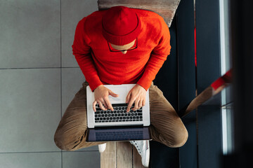Above view of young freelancer man in glasses wear red hat and wool sweater sitting on bench next...