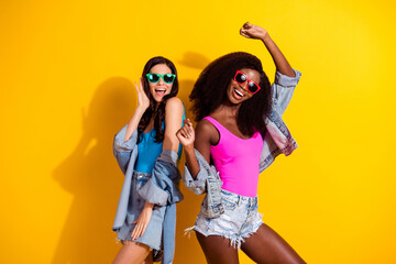 Photo of two funky cheerful ladies enjoy dance wear sunglass top jeans outfit isolated yellow color...