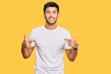 Young handsome man wearing casual white tshirt looking confident with smile on face, pointing...