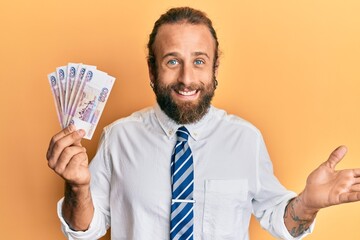 Handsome business man with beard and long hair holding russian 500 ruble banknotes celebrating achievement with happy smile and winner expression with raised hand