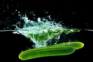 Fototapeta premium Cucumbers falling into the water with a splash againsty black background