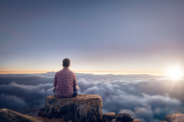 Man sitting on a summit above the clouds during sunrise