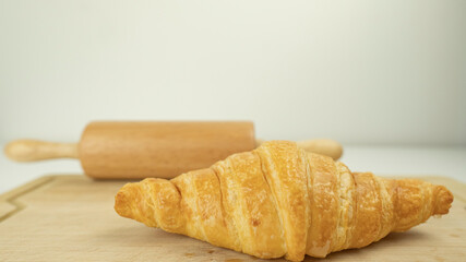 Freshly baked croissants and Rolling pin on wooden cutting board, White background. Crescent-shaped bread originated in France. The popular breakfast menu spread all over the world.