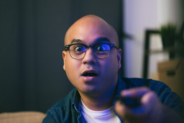 Young asian man watching television using remote to change the program. He very enjoy and excited. He's in living room sitting on sofa.