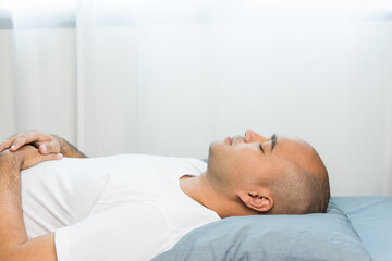 Obraz na płótnie Canvas An Asian bald man around the age of 30 in a white T-shirt is sleeping on a blue mattress and pillows. He slept at home until morning.