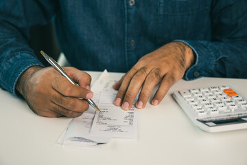 Young man was using a calculator to calculate his income and expenses. In his hand there were bills...