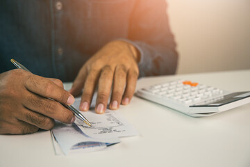Young man was using a calculator to calculate his income and expenses. In his hand there were bills...