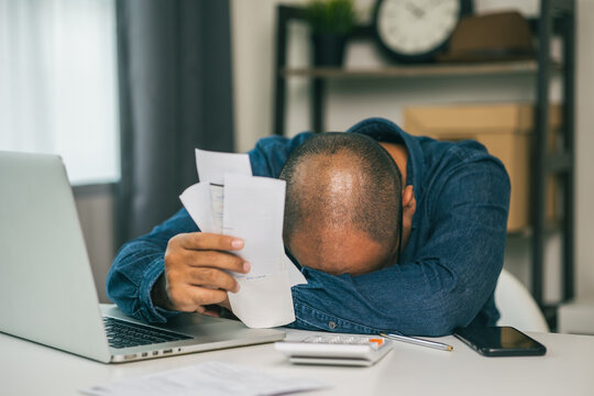 A young Asian man is stressed because he looks at many expense bills and he has no money to pay them. He doesn't know what to do.