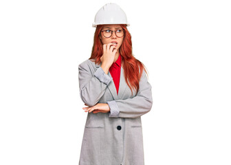 Young redhead woman wearing architect hardhat looking stressed and nervous with hands on mouth biting nails. anxiety problem.