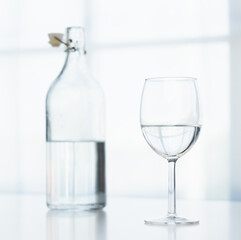 A glass of water and a clear glass water bottle are placed on the table in the house on a white background.