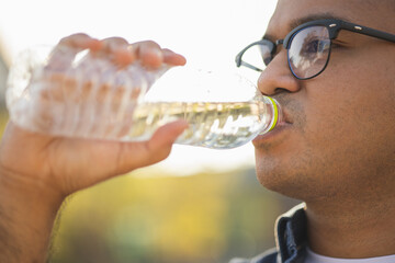 Young asian man drinking cool water from bottle of water in the park.