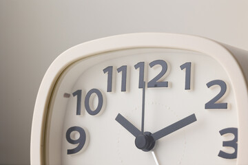 Small white alarm clock, black numbers, set the time for 10.10 o'clock, placed on a white table.