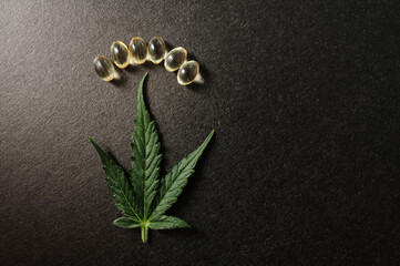 Medicinal cannabis leaves with cbd oil. Marijuana oil in medical capsules isolated on black background.