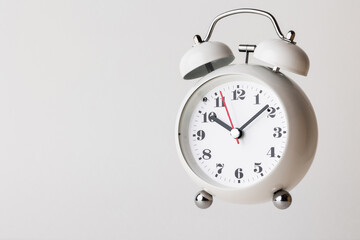 Small white alarm clock, black numbers, set the time for 10.10 o'clock, placed on a white table.