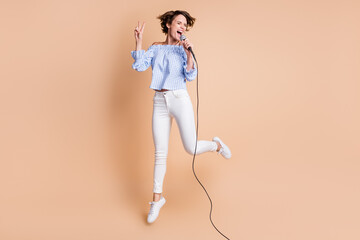Full length photo of young crazy girl happy sing microphone jump up show cool peace v-sign isolated...