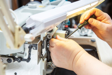 Female hands with a screwdriver repair the shuttle of the sewing machine.