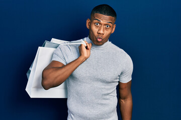 Young black man holding shopping bags scared and amazed with open mouth for surprise, disbelief face