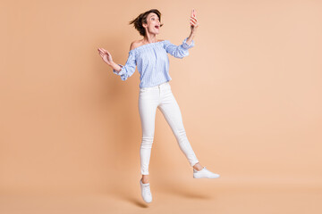 Full length body size view of lovely amazed cheerful girl jumping using gadget having fun isolated over beige pastel color background