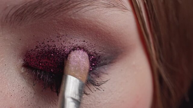 Professional makeup. The makeup artist applies the glitter to the model's eyelid with a brush. Extreme close-up of the eye.