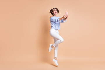 Fototapeta na wymiar Full length photo of young excited girl happy positive smile jump make selfie record video blogger isolated over beige color background
