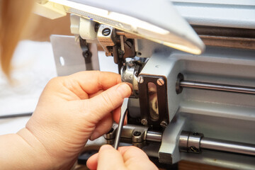 Female hands with a screwdriver repair the shuttle of the sewing machine.