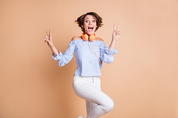 Portrait of lovely amazed cheerful girl showing double v-sign having fun isolated over beige pastel color background