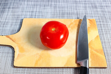 There is a whole red tomato on the chopping board and a knife next to it.