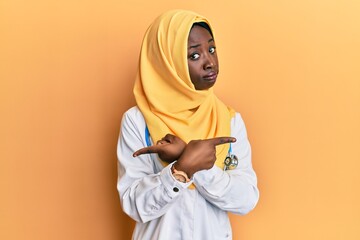 Beautiful african young woman wearing doctor uniform and hijab pointing to both sides with fingers, different direction disagree