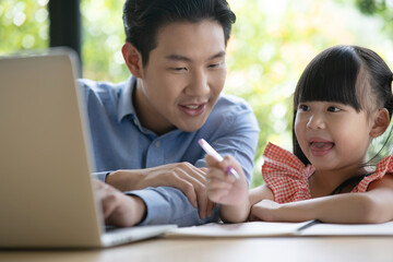 Young Asian dad wearing a blue shirt enjoys teaching his lovely daughter do a homework on a laptop. Asian little girl kind enjoy learning with her father