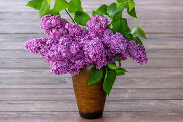 Bouquet purple (Violet) Lilac Flower  in a brown vase a wooden surface. Syringa vulgaris (common lilac). Spring flowers.