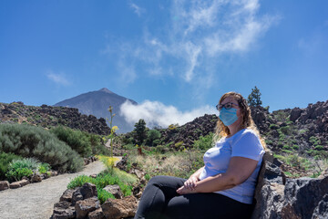 Young tourist woman sitting with mask in Teide National Park. In the background is the Teide. This volcano is located in Tenerife, Canary Islands. © AventurasxCanarias
