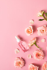 Bottles of serum with rose flowers flat lay on pink background