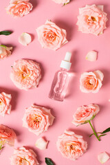 Bottles of serum with rose flowers flat lay on pink background