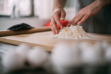 A male chef prepares noodle dough at home in the kitchen. Close up of hands with flour and dough