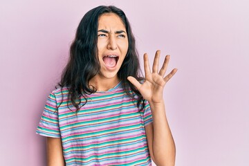 Hispanic teenager girl with dental braces wearing casual clothes shouting and screaming loud to side with hand on mouth. communication concept.