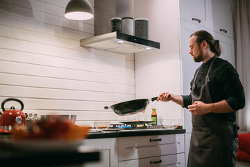 A male cook is cooking at the stove at home in the kitchen