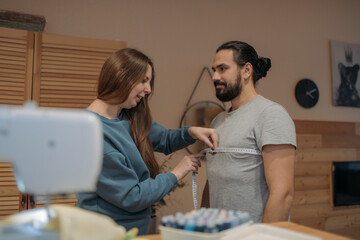 A young woman takes measurements from a man for sewing clothes