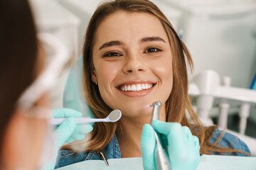 Smiling woman sitting in medical chair while dentist fixing her teeth