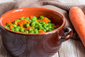 Green peas and carrots in small pan on wooden background.