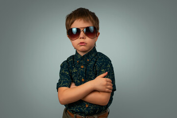 A little boy in sunglasses and a bright shirt. Grey background in the studio