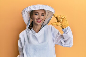 Beautiful blonde caucasian woman wearing protective beekeeper uniform smiling and confident...