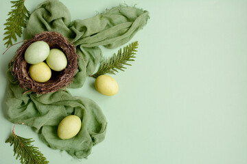 Easter celebration. Layout of colored eggs in the nest on a green napkin on a light green background. Top view, copy space