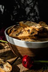 Homemade almond and chocolate biscotti with glass of coffee and  ranunculus flowers on wooden table on dark background.