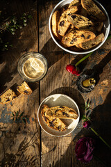 Homemade almond and chocolate biscotti with glass of coffee and  ranunculus flowers on wooden table on dark background.